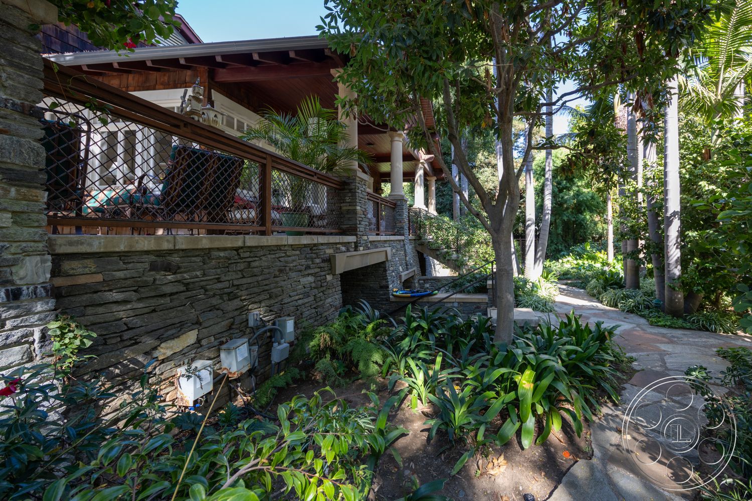 Americana 48 - stone accent wall, surrounding greenery, exposed wooden beams, lush tropical landscaping, flagstone pathway, wooden deck railing, interior patio area, natural stone landscaping, gabled roof structure, residential outdoor setting
