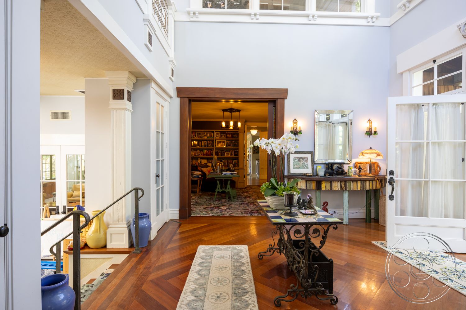 Americana 48 - neutral color palette, hardwood flooring, open floor plan, area rug, arched doorways, textured plaster walls, large floor-to-ceiling windows, flower arrangement, built-in cabinetry, ornate entryway, elegant foyer, crown molding details, glass panel doors, decorative wall sconce lighting, vintage decor accents, herringbone pattern hardwood floors, custom wood furniture