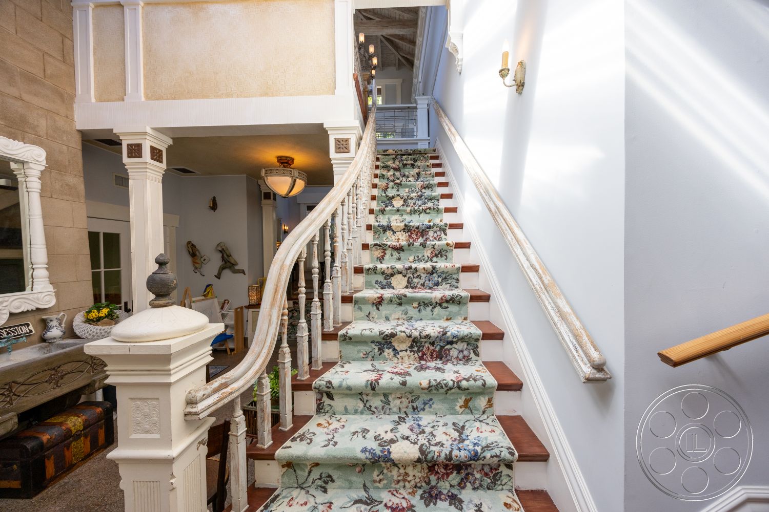 Americana 48 - neutral wall colors, textured wall finish, arched doorways, curved staircase, decorative wall molding, vintage light fixture, exposed wood ceiling beams, decorative wall mirror, hardwood stair treads, carpeted stair runners with floral pattern, white painted railing