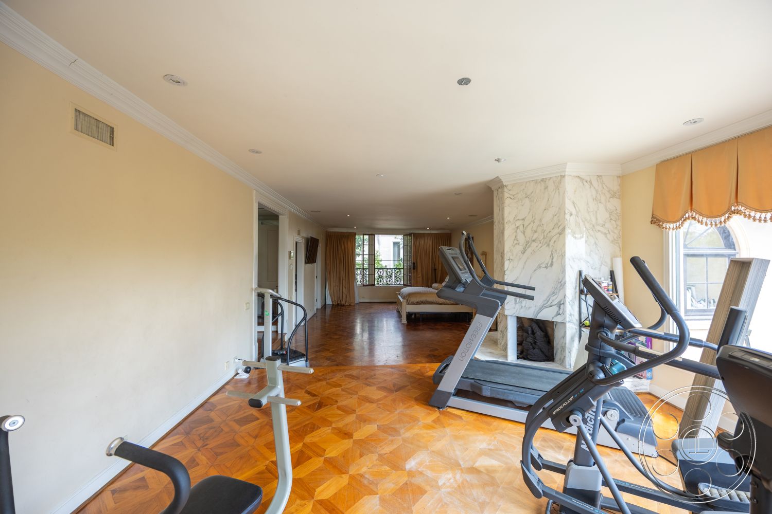 Mansion 146 - open layout, exercise equipment, modern aesthetic, floor-to-ceiling windows, marble fireplace surround, parquet hardwood flooring, crown molding details, plain painted walls, drapery window treatments, working out area