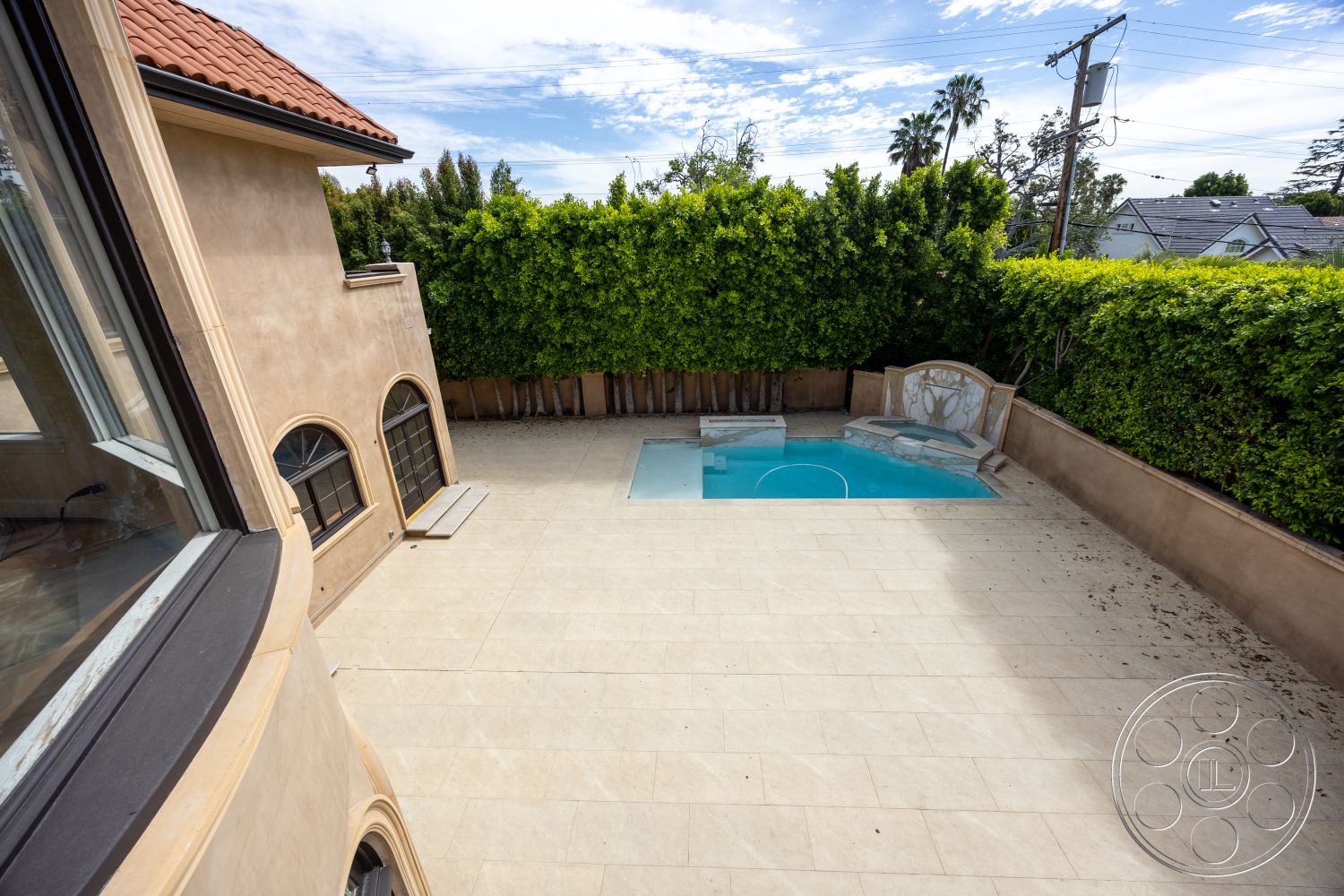 Mansion 146 - exterior, landscaped surroundings, arched windows, rectangular pool, clay tile roof, stone pool deck, tile patio flooring, residential backyard setting, plastered beige walls, large stone pool steps, lush green hedge, paved pool area