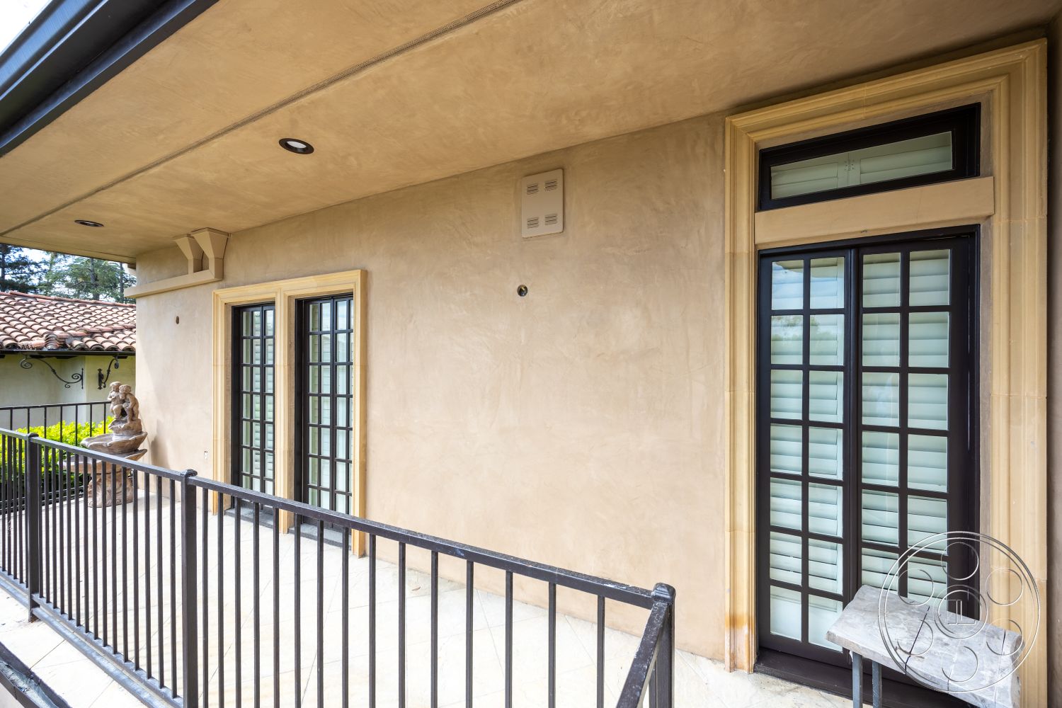 Mansion 146 - exterior, black metal railing, outdoor lighting fixtures, slate tile flooring, stucco wall finish, decorative stone statue, double door with black grille, covered balcony area, wooden doorframe detailing, overhanging eave