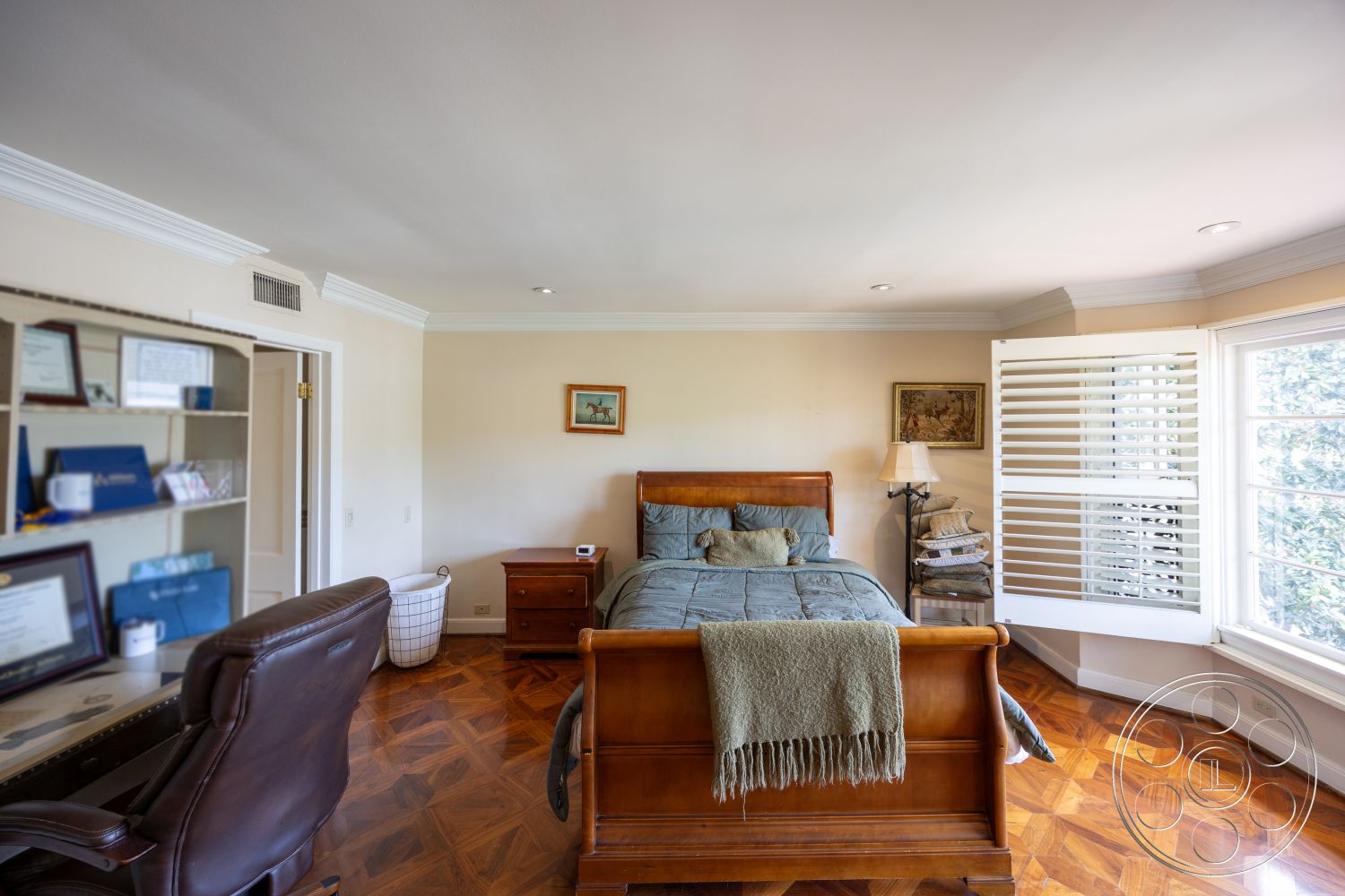 Mansion 146 - textured area rug, wooden nightstand, hardwood bedroom floors, crown molding details, beige painted walls, detailed wall art, contemporary desk chair, king-size wooden bed frame, large bay window with shutters, upholstered accent pillows