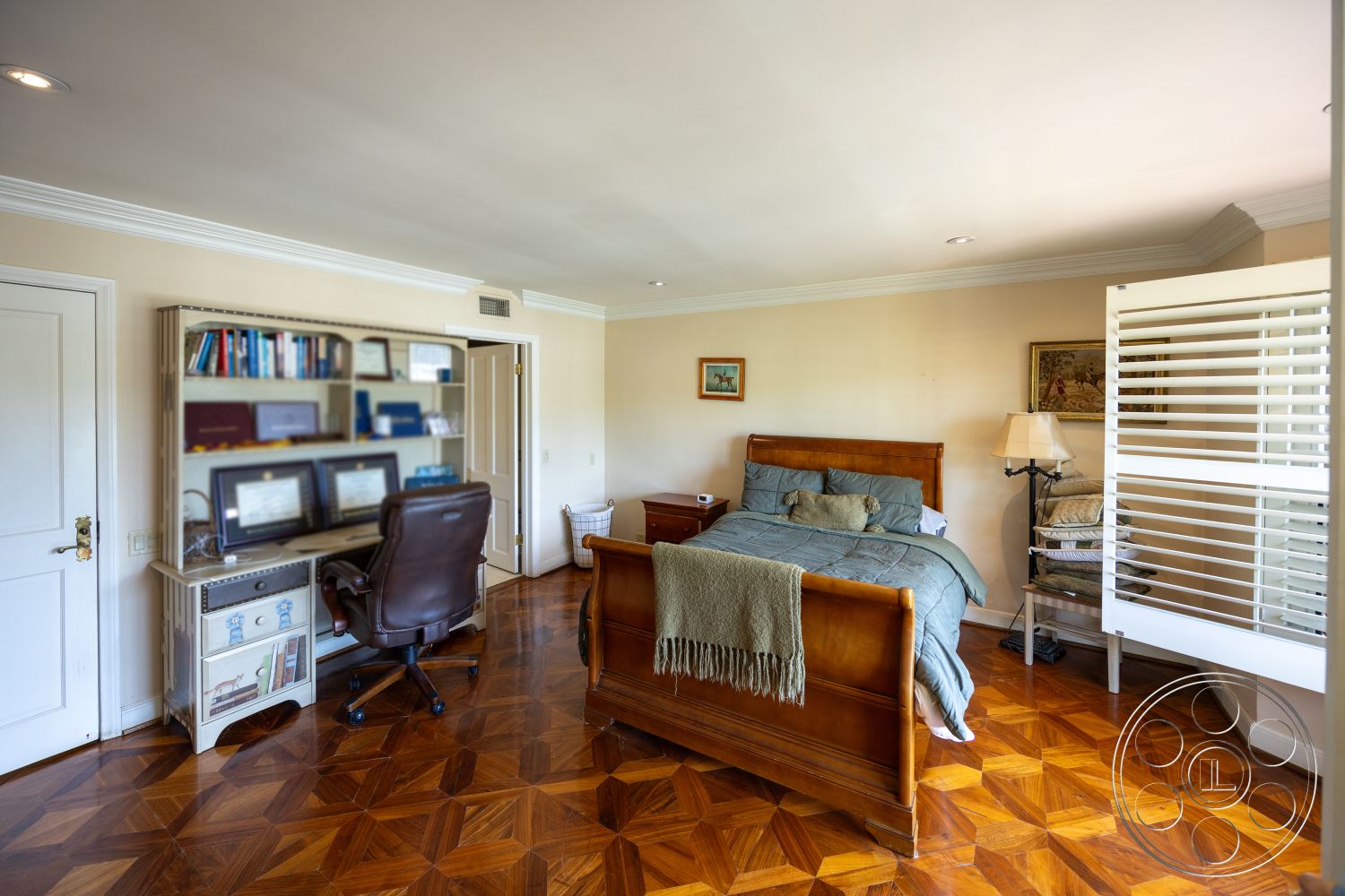 Mansion 146 - glass table lamp, white painted walls, decorative throw blanket, crown molding details, framed artwork on walls, leather office chair, hardwood chevron-pattern bedroom flooring, queen-size wooden bed frame, open shelving unit with books, folding wooden room divider