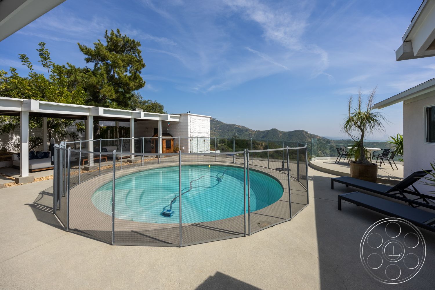Retro 288 - exterior, glass railing, modern outdoor furniture, concrete pool deck, round swimming pool, landscaped garden area, concrete patio floor, wooden pergola structure, mountain view backdrop, potted palm plants, metal pool safety fence