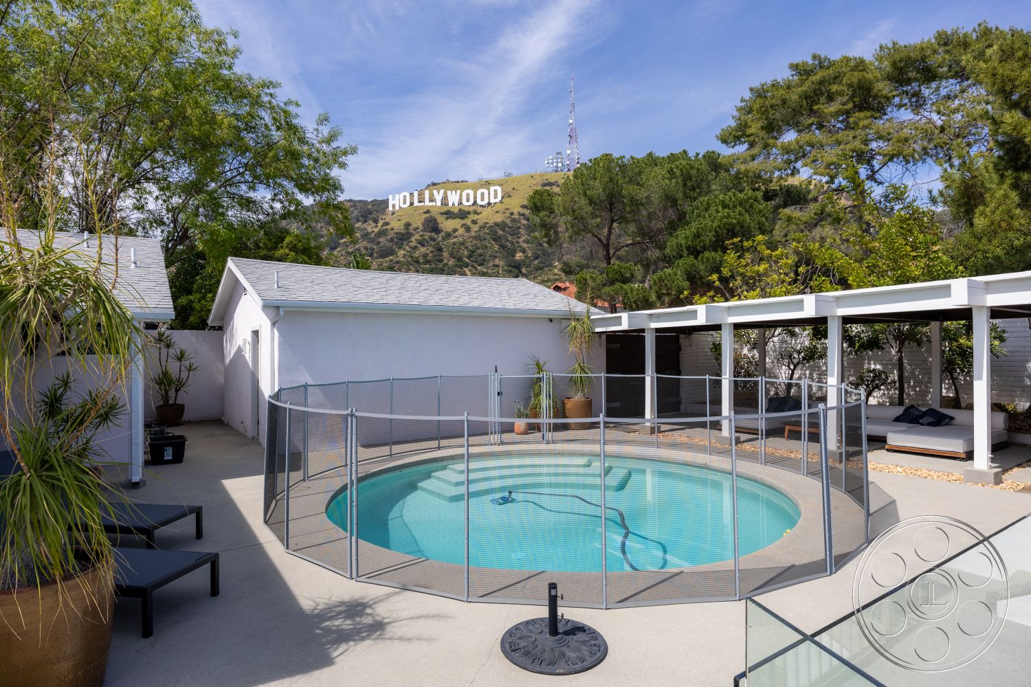 Retro 288 - exterior, green landscaping, single-story home, decorative planters, mountain view, sloping roof, tile roof, wooden overhang, circular pool, concrete patio flooring, modern outdoor seating area, glass pool safety fence, Hollywood sign view