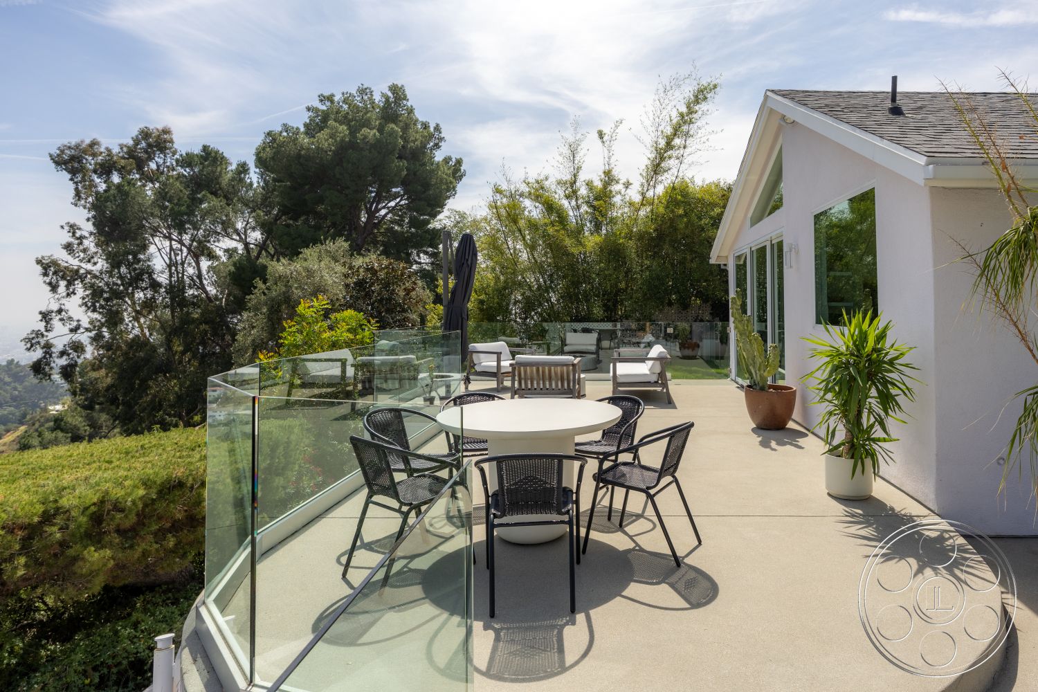 Retro 288 - large windows, exterior, landscaped garden, flat roof, glass railing, round dining table, open outdoor space, black metal chairs, mountain view, modern house, concrete patio flooring, white painted walls, sloped green lawn