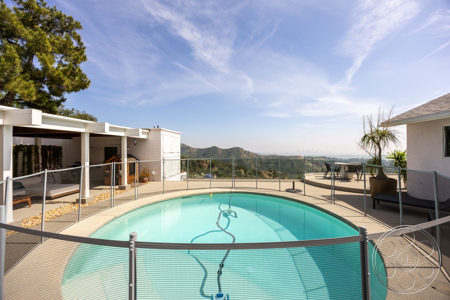 Retro 288 - glass pool fence, modern outdoor seating, light-colored exterior walls, oval pool, mountain view setting, concrete patio flooring, landscaped garden with stone accents, covered patio with exposed beams