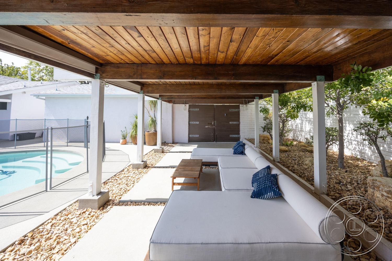 Retro 288 - exterior, wooden coffee table, sliding glass doors, tropical plants, rectangular swimming pool, glass pool fence, modern outdoor seating, landscaped garden area, concrete patio flooring, wood beam ceiling, white painted walls, decorative rock garden, fenced pool area