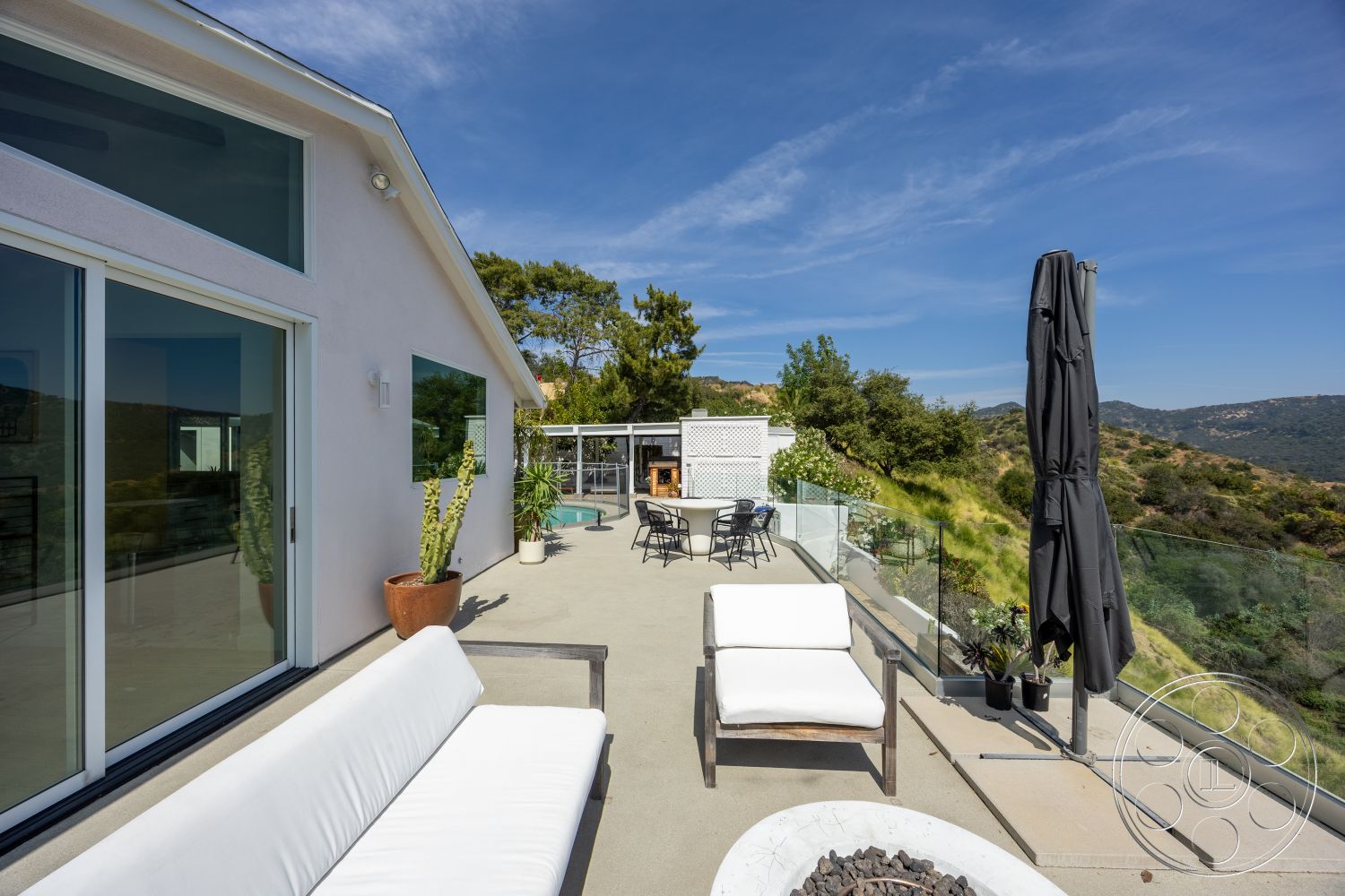 Retro 288 - exterior, large floor-to-ceiling windows, white sofa, contemporary outdoor space, outdoor umbrella, concrete patio flooring, open outdoor seating area, landscaped hillside view, modern glass railing, desert plant accents, wood framed chairs, minimalist fire pit, applied stucco wall finish