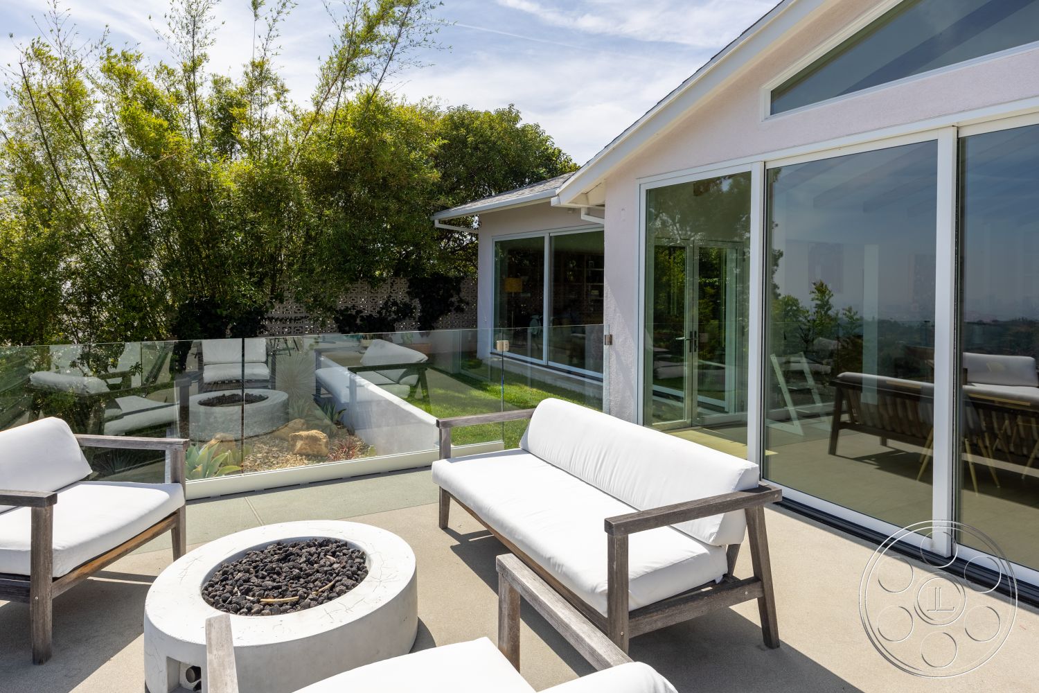 Retro 288 - exterior, large glass sliding doors, bamboo landscaping, modern home design, flat roof structure, concrete patio floor, rectangular fire pit, framed glass railing, white upholstered outdoor chairs, concrete fire pit with lava rocks