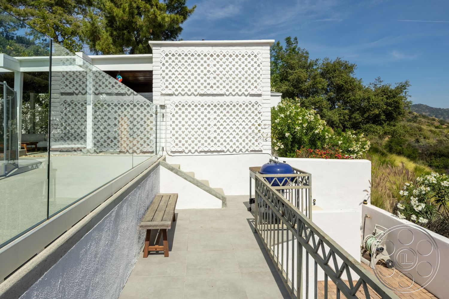 Retro 288 - exterior, white stucco walls, glass railing, mountain view, landscaped garden area, concrete patio flooring, wood bench seating, gray concrete steps, decorative lattice wall, blue barbecue grill, greenery with flowering plants