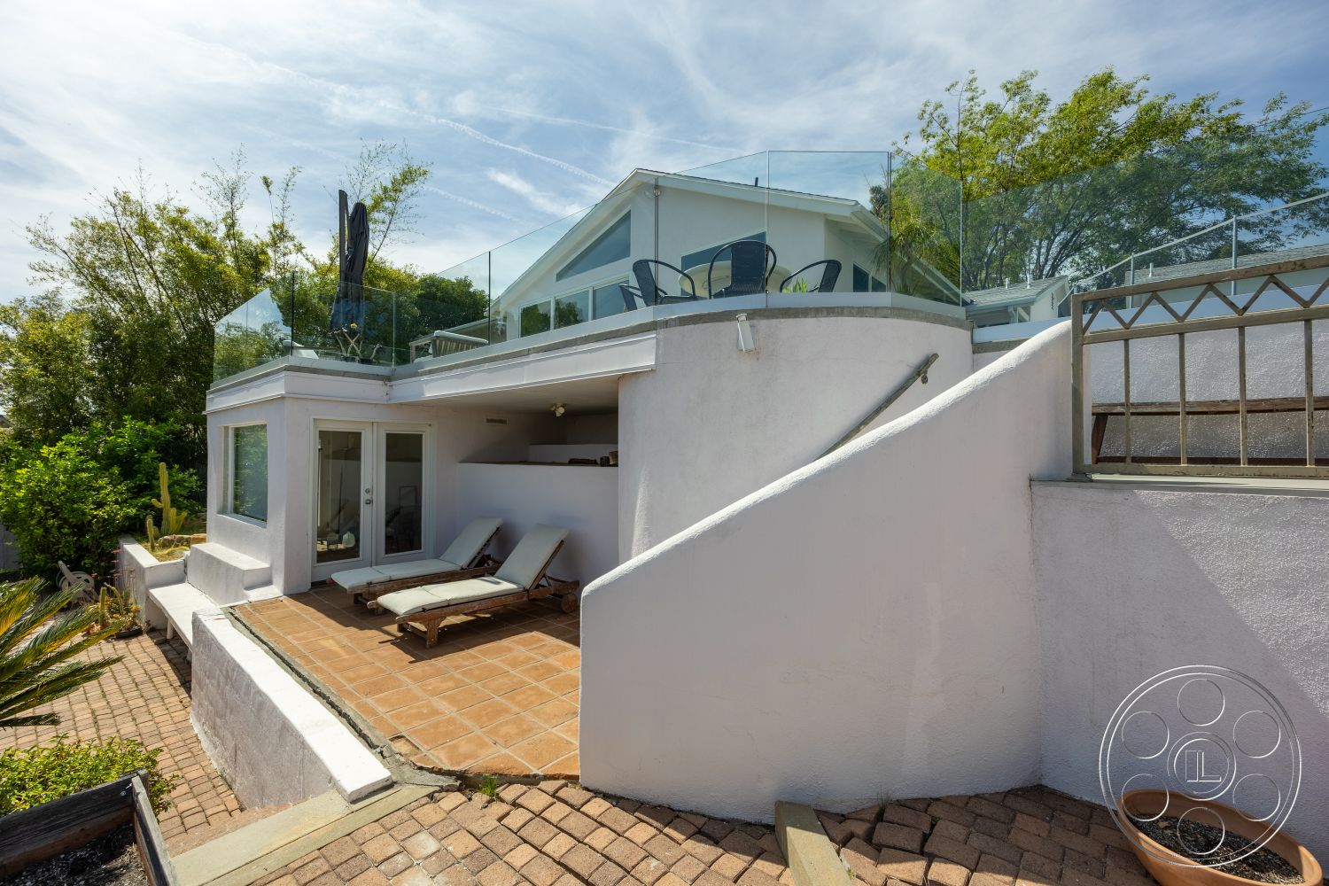 Retro 288 - exterior, white stucco walls, glass railing, sloping terrain, concrete steps, outdoor lounge area, surrounded by greenery, landscaped garden setting, modern outdoor seating area, terracotta patio flooring, brick paver pathway, flat roofline