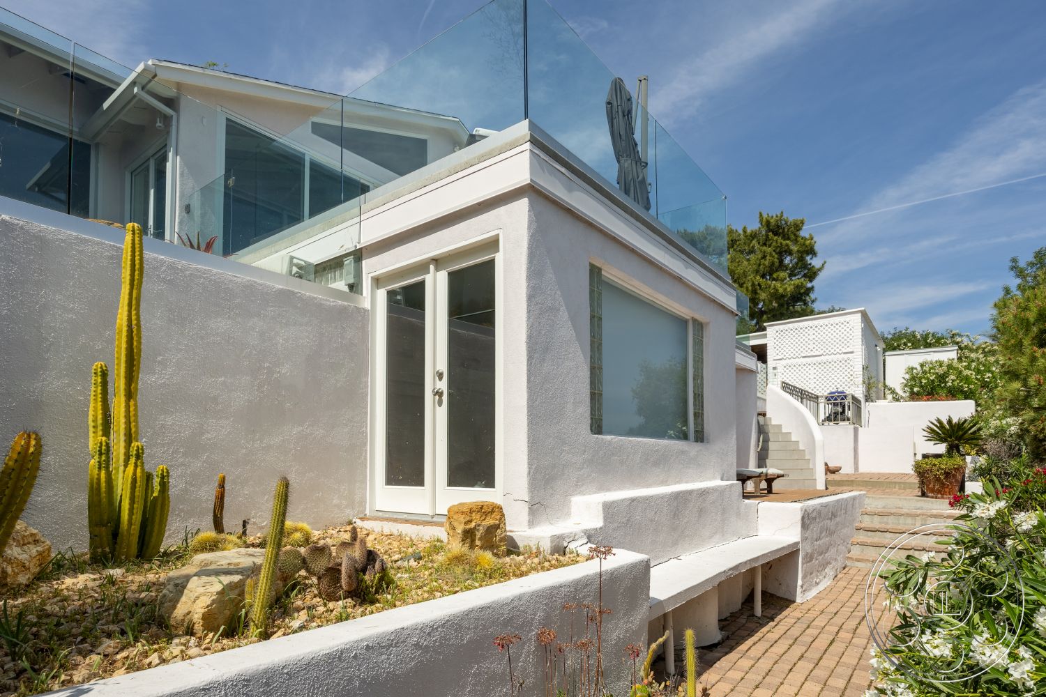 Retro 288 - exterior, minimalist aesthetic, large glass windows, outdoor seating area, glass railing, open-air design, desert landscaping, concrete retaining wall, flat roof design, contemporary architectural style, stucco wall finish, paver patio flooring, succulent plant arrangement, integrated bench seating, step access to upper level