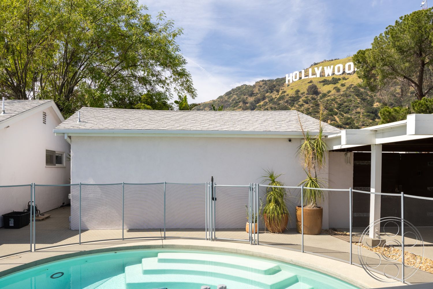 Retro 288 - exterior, white stucco walls, potted plants, metal fence, mountain backdrop, concrete pool deck, hardscape patio, shingle roof, landscaped garden area, glass pool fencing, Hollywood sign view, kidney-shaped pool
