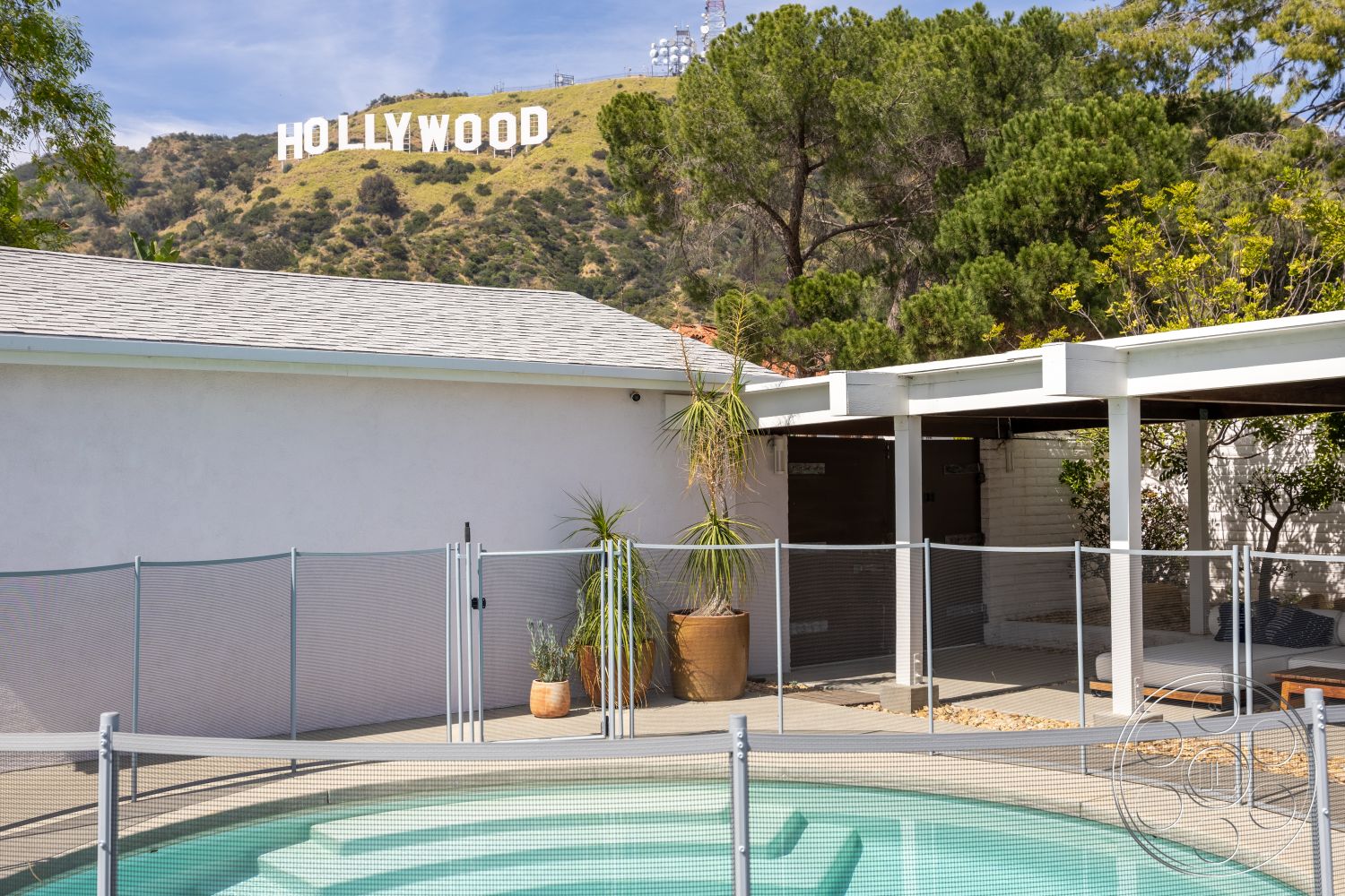 Retro 288 - exterior, landscaped garden, stucco walls, tiled roof, glass pool fence, concrete pool deck, large potted plants, sloped hillside setting, Hollywood sign view, kidney-shaped pool, wooden patio cover