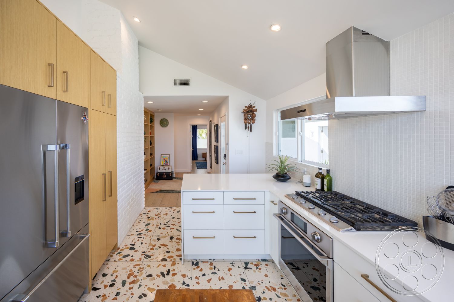 Retro 288 - modern kitchen, natural light, terrazzo flooring, open floor plan, stainless steel appliances, wood cabinetry, kitchen island, floor-to-ceiling windows, exposed brick wall, high vaulted ceiling, gas range, hood vent, white quartz countertops, drawer pulls