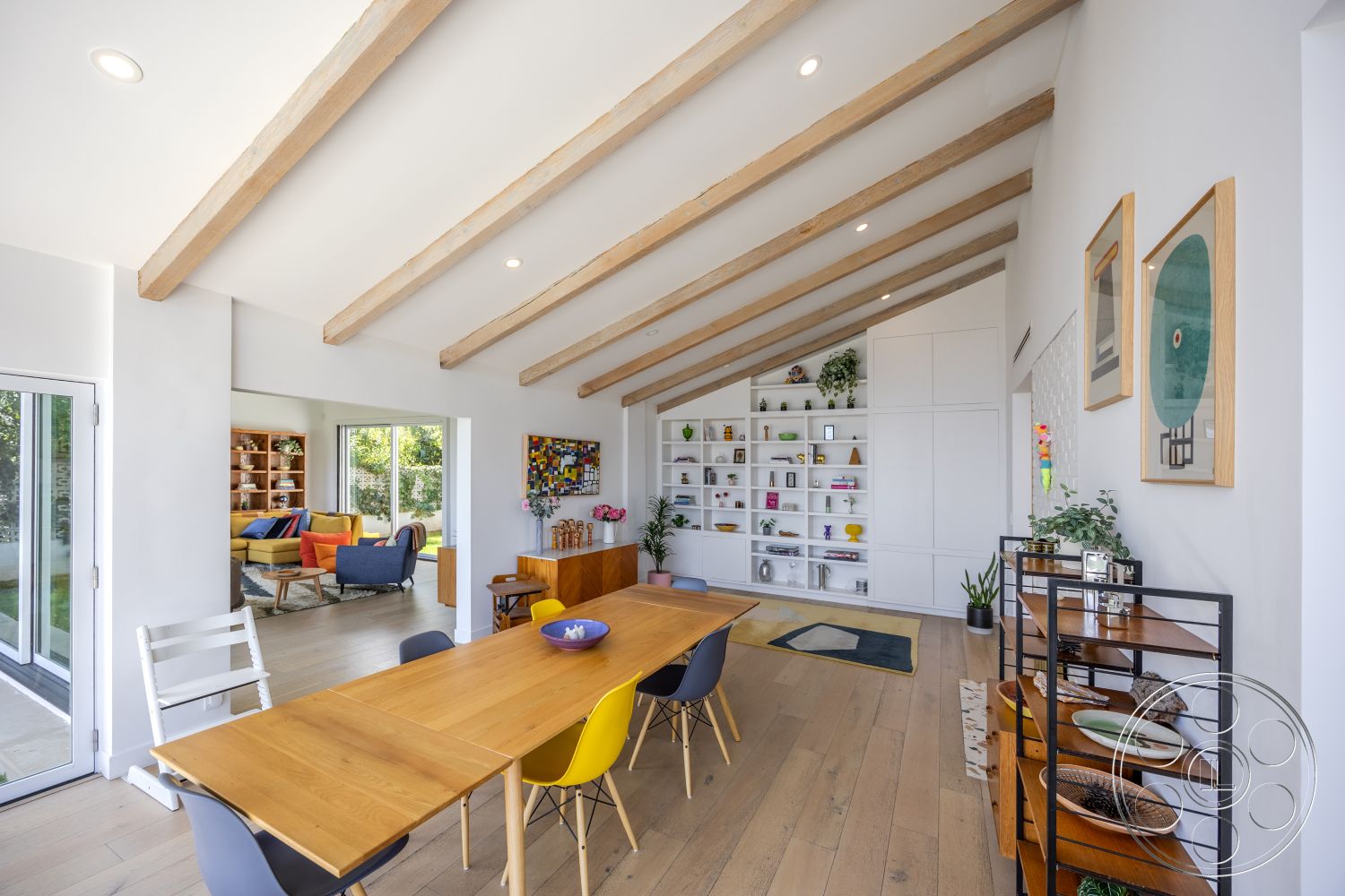 Retro 288 - light hardwood flooring, open floor plan, functional workspace, green indoor plants, natural light from large windows, efficient layout, modern dining area, multicolored throw pillows, exposed wood ceiling beams, white painted walls, built-in shelving unit, cozy living area, rectangular wooden dining table, contemporary accent decor, colorful dining chairs