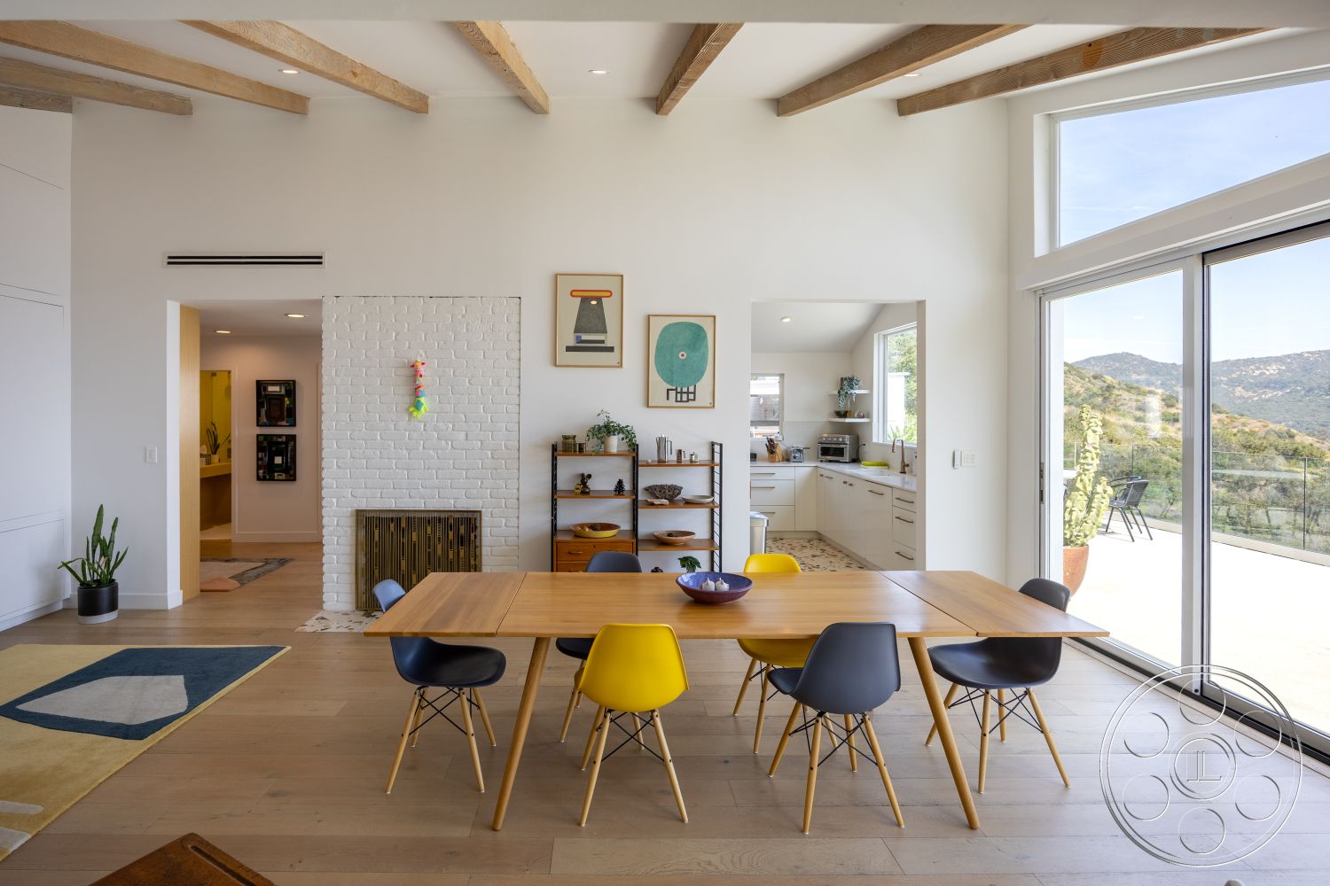 Retro 288 - open floor plan, glass sliding doors, mountain view, modern dining table, exposed wood ceiling beams, brick fireplace surround, white painted walls, hardwood dining room floors, Eames-style dining chairs