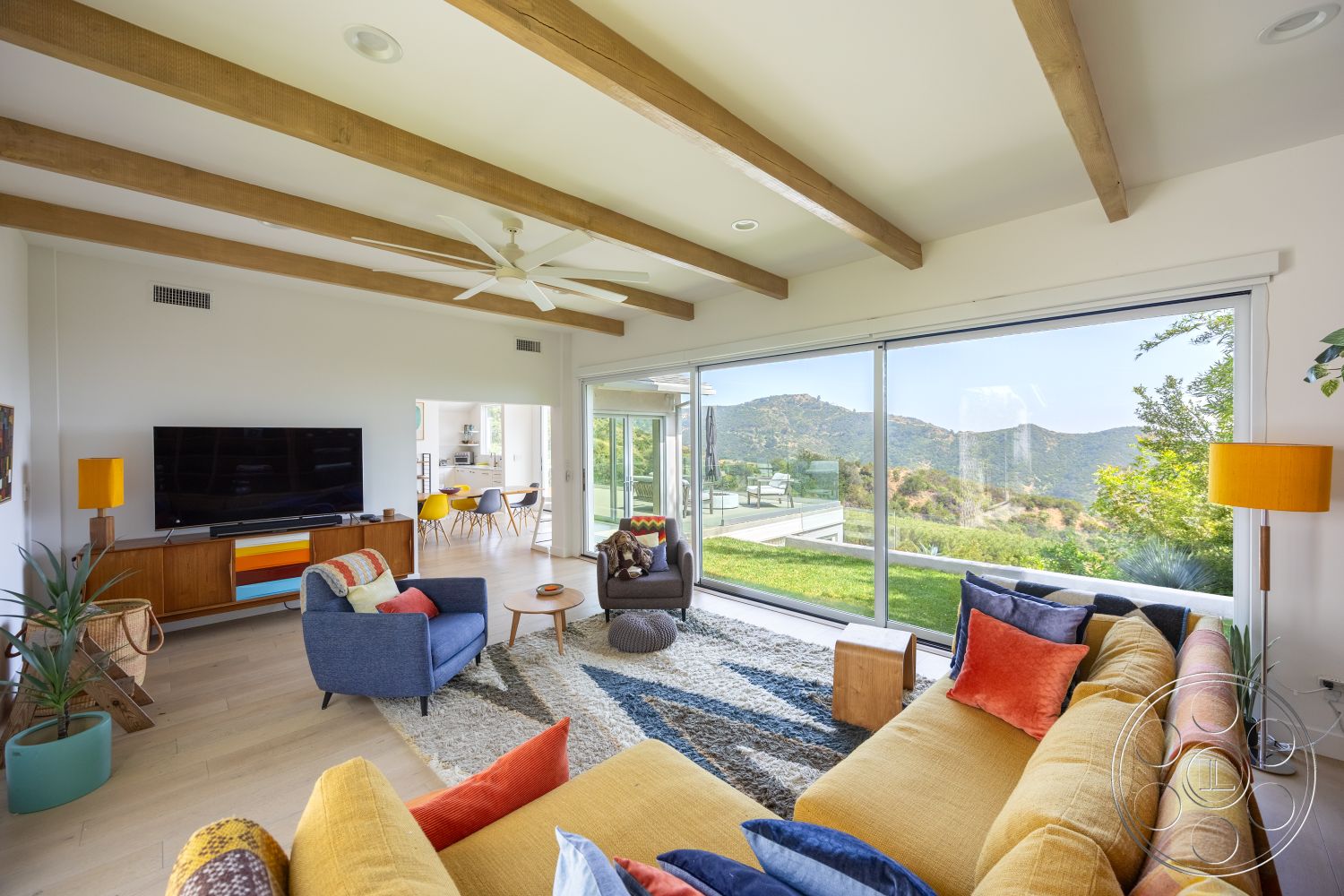 Retro 288 - large windows, natural light, open floor plan, glass sliding doors, mountain view, decorative indoor plant, colorful throw pillows, mid-century modern furniture, plush area rug, flat-screen television, contemporary coffee table, exposed wood ceiling beams, hardwood living room floors, modern sofa, yellow accent lamp