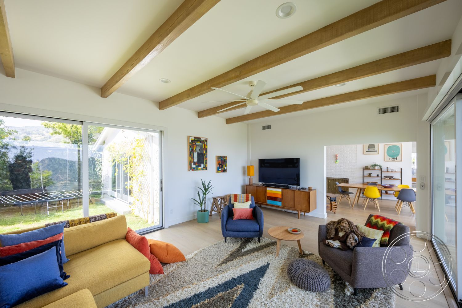 Retro 288 - living room, textured area rug, contemporary furniture, open floor plan, modern art wall decor, colorful accent pillows, plant decoration, large sliding glass doors, mid-century modern style, hardwood living room floors, wood beam ceiling, white painted walls