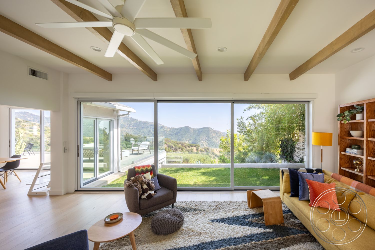 Retro 288 - exterior, wood coffee table, modern furniture, wooden bookshelf, plush area rug, light wood floor, stylish accent chair, mountain view setting, vaulted ceiling with exposed wood beams, large floor-to-ceiling glass sliding doors, contemporary living room design, yellow upholstered sofa, suburban hillside location