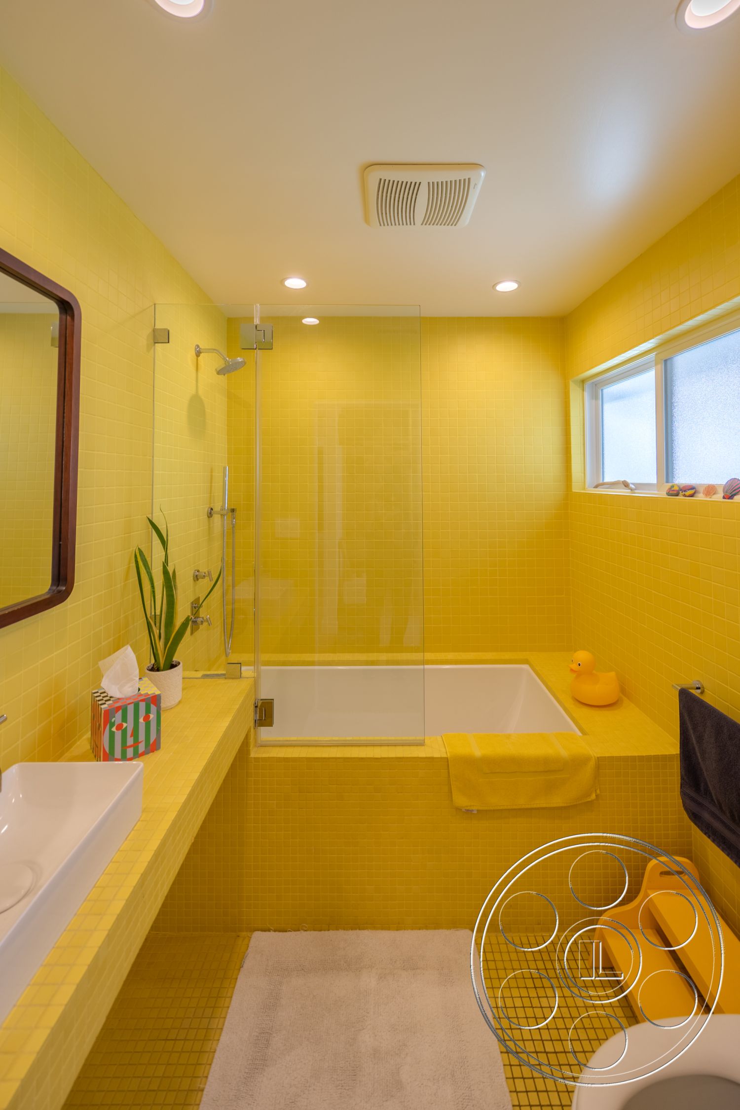 Retro 288 - glass shower enclosure, sliding window, yellow bath towel, recessed ceiling lighting, rectangular soaking tub, wood framed mirror, yellow tiled bathroom walls, yellow mosaic tile flooring, modern bathroom sink, white bath mat, plant in ceramic pot, bathroom countertop, white tissue box, exposed ceiling vent