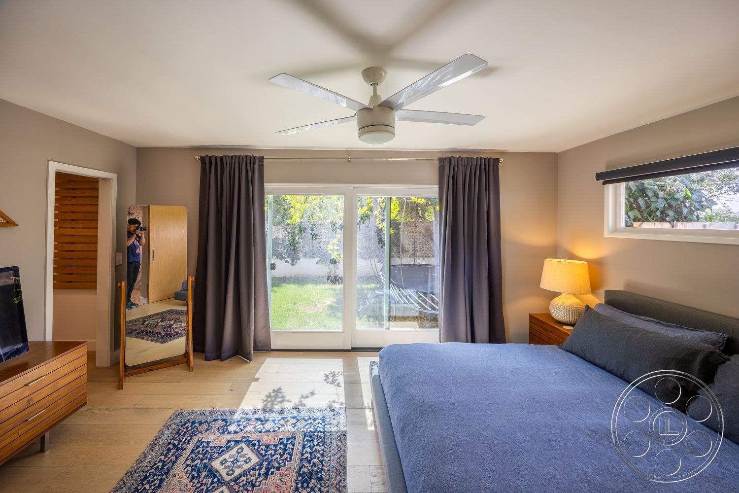 Retro 288 - natural light, textured area rug, floor-to-ceiling windows, dark wood furniture, large sliding glass doors, modern ceiling fan, hardwood bedroom floors, gray painted walls, curtain window treatments, mirror with wooden frame, blue upholstered bed