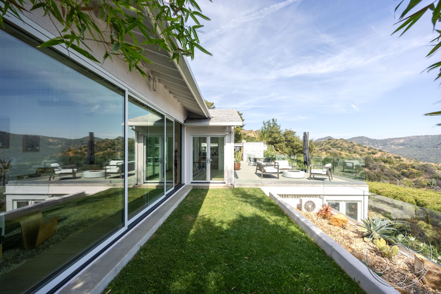 Retro 288 - exterior, wooden deck, metal railing, grassy lawn, modern architectural style, sloped landscape, flat roof design, landscaped garden area, concrete patio flooring, glass wall panels, surrounding hillside setting, clear panoramic view