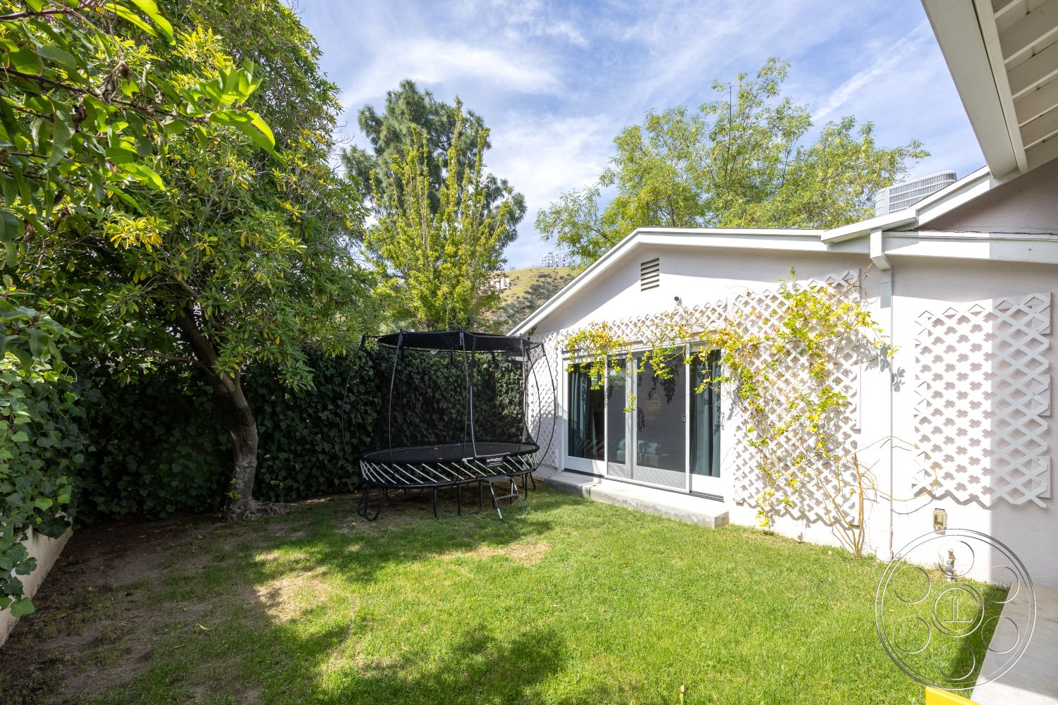 Retro 288 - exterior, landscaped garden, mature trees, sloped roof, trampoline, large sliding glass doors, surrounding shrubbery, white stucco house walls, outdoor grass lawn, wooden lattice trellis