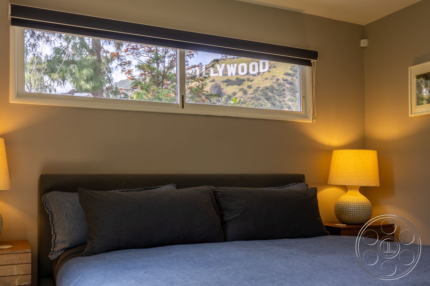 Retro 288 - suburban setting, floor-to-ceiling windows, natural light from windows, wood nightstand, plush gray bedding, gray painted walls, modern upholstered bed, table lamp with fabric shade, Hollywood sign view, decorative wall frame