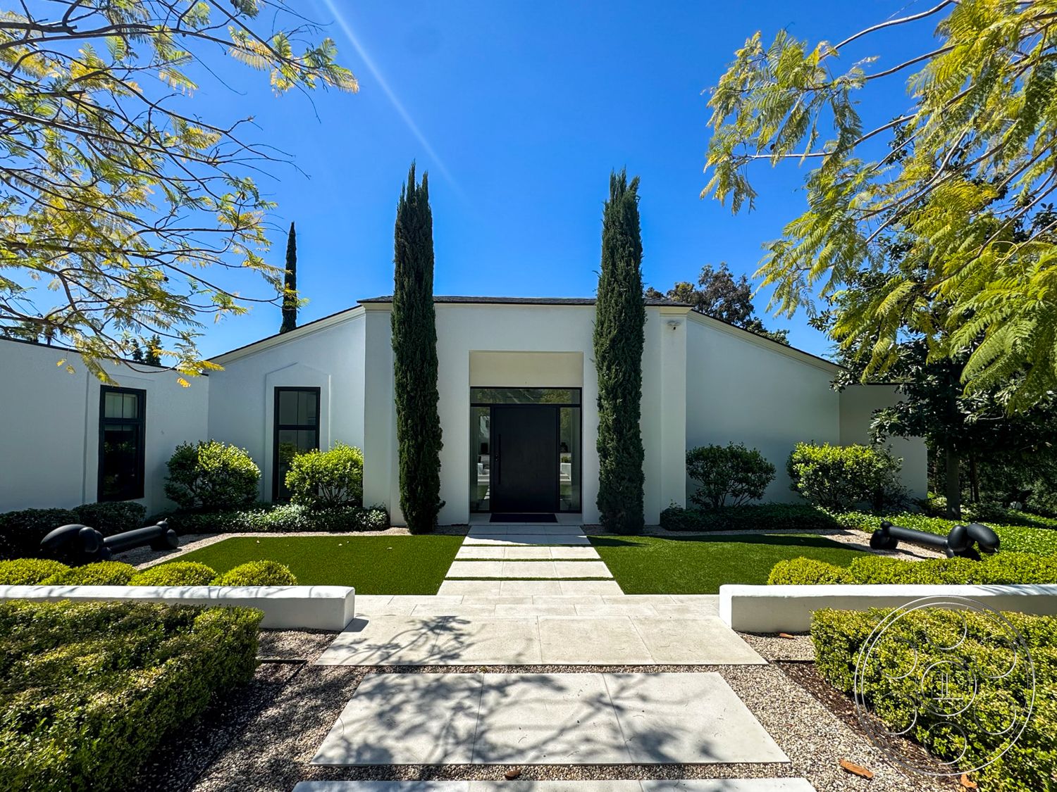 Modern 522 - exterior, white stucco walls, flat roof, concrete pathway, open lawn area, black window frames, tall cypress trees, boxwood hedges, symmetrical landscaping, drought-tolerant plants, sunny outdoor setting, modern minimalist design, rectangular concrete pavers, gravel garden beds, centered front entrance, large black front door