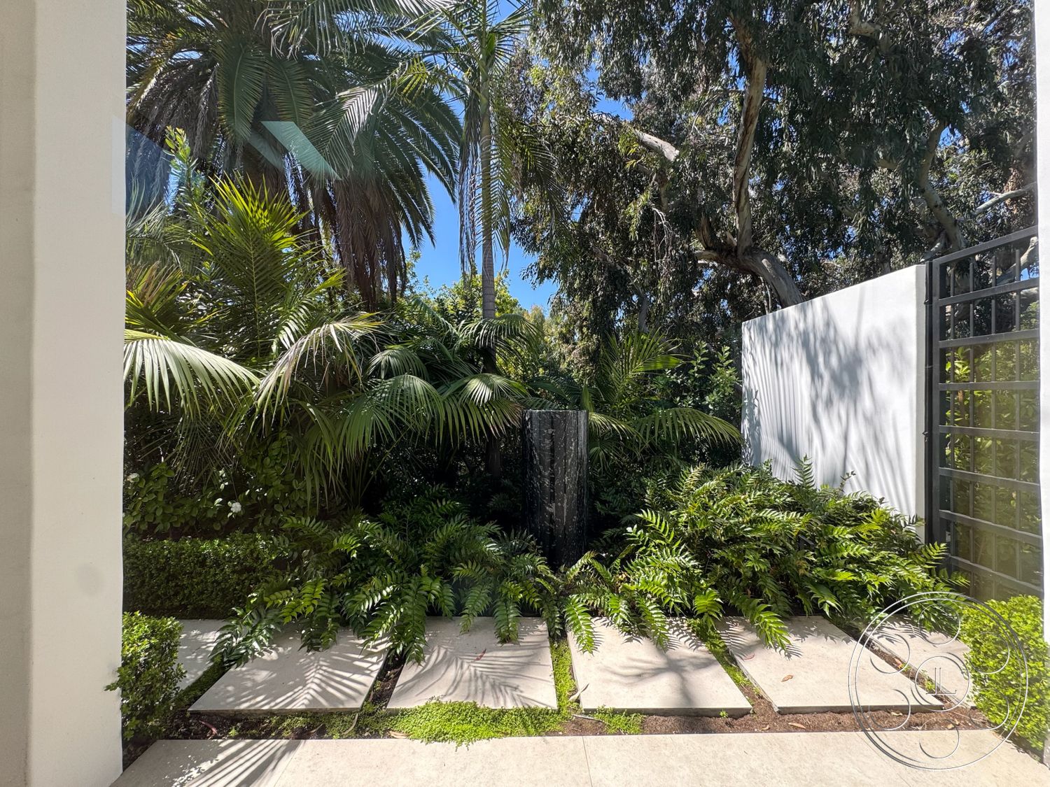 Modern 522 - exterior, lush tropical landscaping, tall palm trees, white stucco wall, concrete stepping stones, well-maintained shrubbery, green ferns, modern stone feature wall, decorative metal fence, natural stone garden area