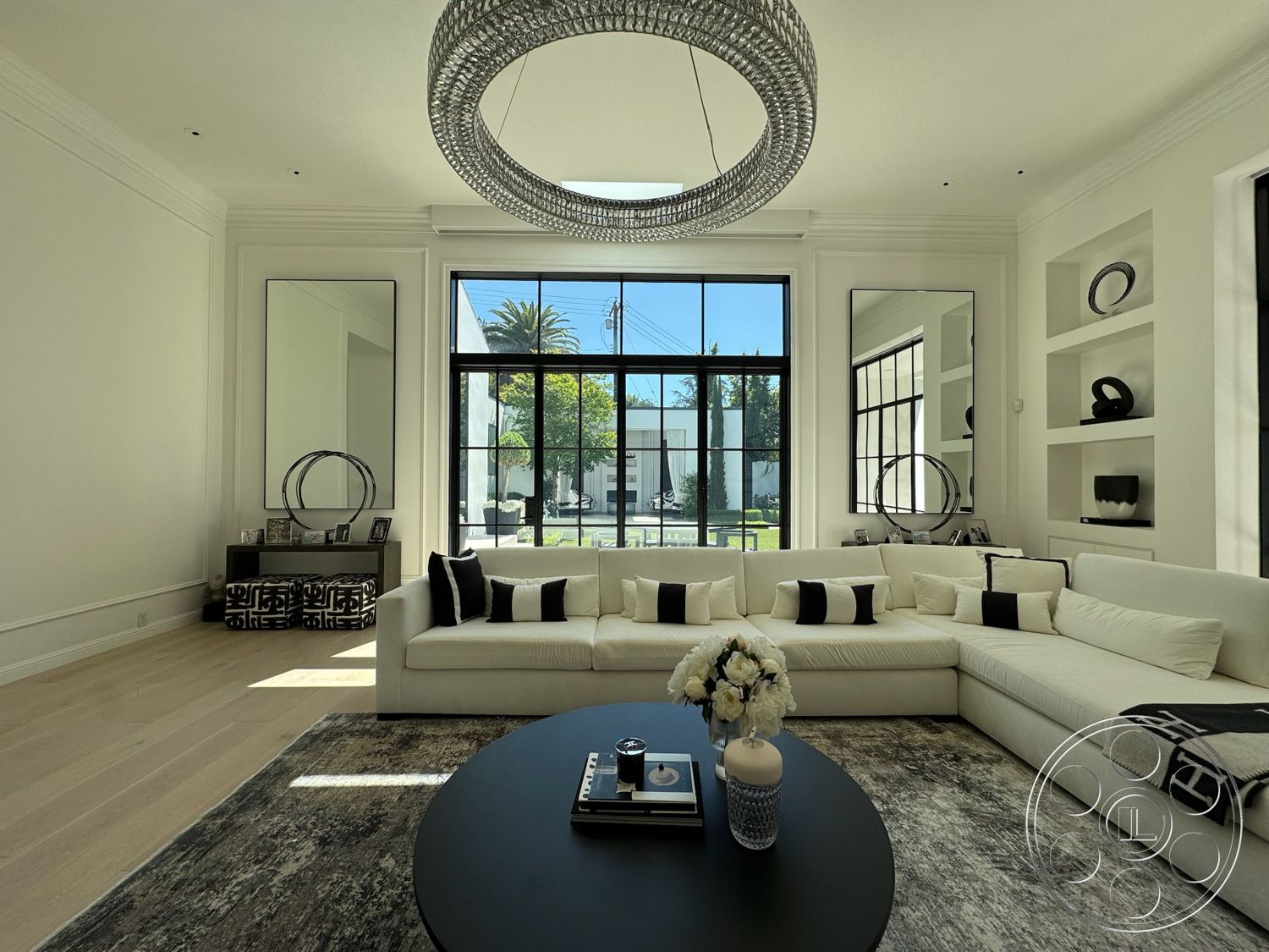Modern 522 - white walls, minimalist decor, natural light, contemporary style, textured area rug, light hardwood flooring, open layout, modern chandelier, large floor-to-ceiling windows, black metal window frames, high ceiling living room, black and white accent pillows, sectional sofa with white upholstery, round black coffee table, decorative built-in shelving, polished decorative accents