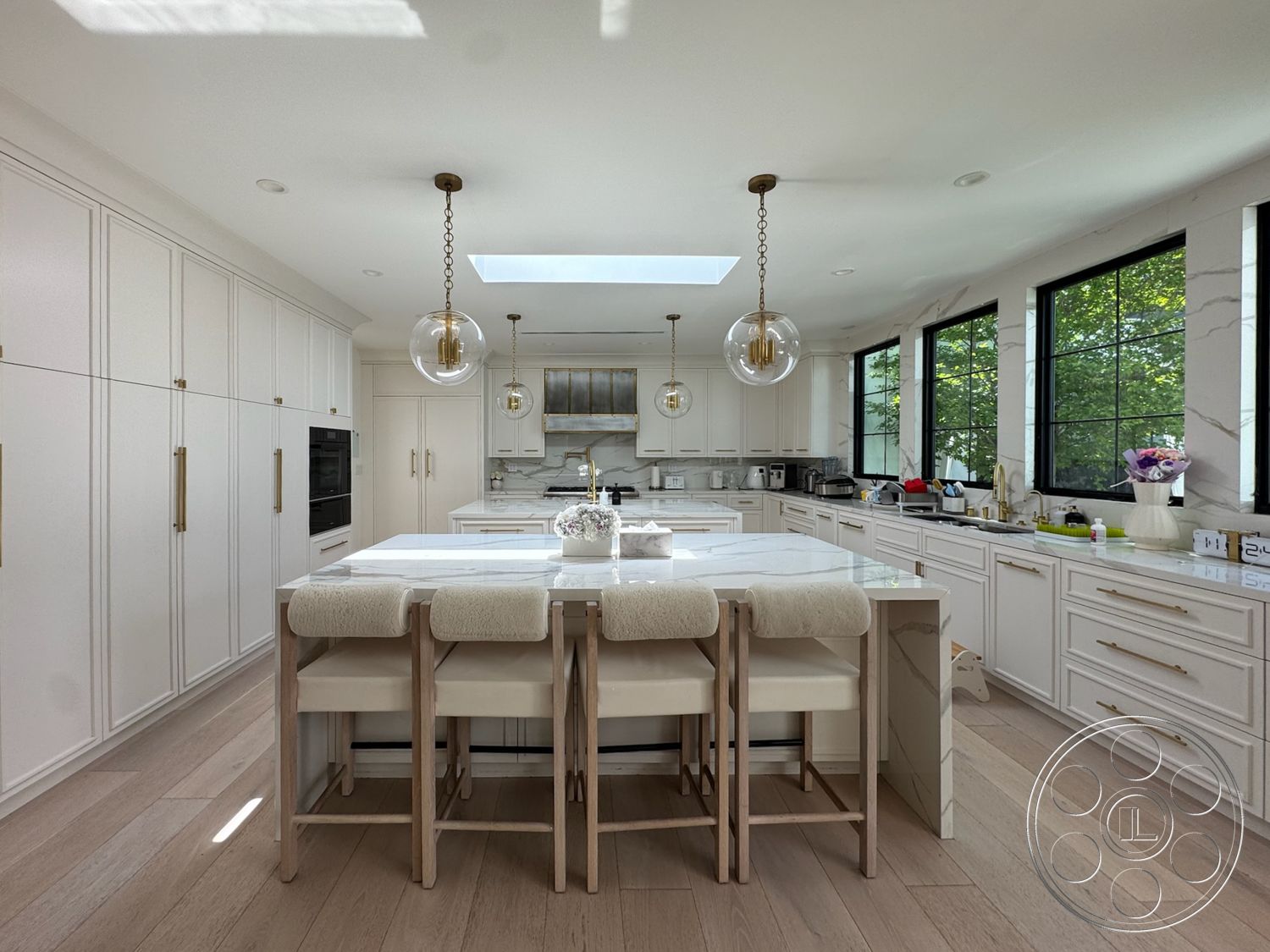 Modern 522 - light-colored walls, open floor plan, white cabinetry, marble countertop, black window frames, glass pendant lighting, modern kitchen design, gold cabinet hardware, built-in kitchen appliances, skylight ceiling, integrated refrigerator, wooden kitchen island, vinyl plank flooring, large kitchen windows