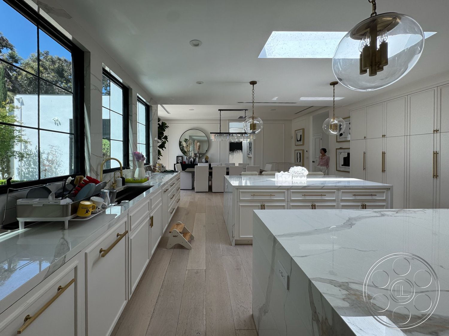 Modern 522 - minimalist decor, neutral color palette, plant accents, modern light fixtures, stone backsplash, skylights, bright and airy atmosphere, large floor-to-ceiling windows, white marble countertops, open concept kitchen, hardwood kitchen floors, white cabinetry with gold hardware, circular mirror accent, stylish kitchen island