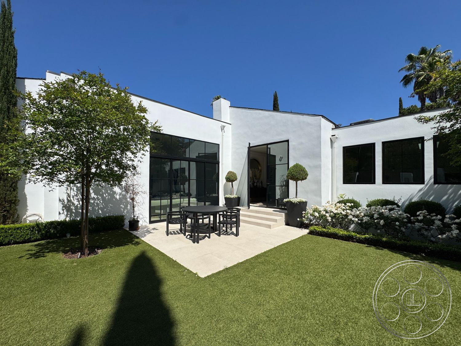 Modern 522 - exterior, white stucco walls, flat roof, minimalist design, large glass sliding doors, surrounding greenery, modern landscaping, topiary shrubs, black metal window frames, clean lines architecture, rectangular outdoor dining table, urban outdoor setting, concrete patio steps, turf grass lawn