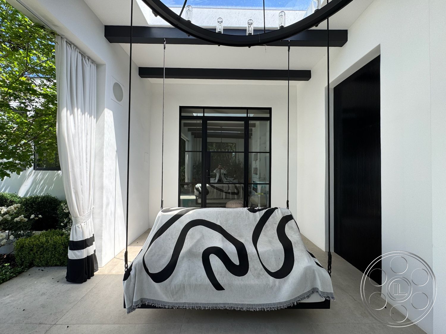 Modern 522 - exterior, modern architectural style, open-air design, white plaster walls, lush green landscaping, concrete patio flooring, covered outdoor area, black steel frame windows, hanging bed with black and white patterned throw, decorative garden bushes, sheer white curtain drapes, overhead circular light fixture