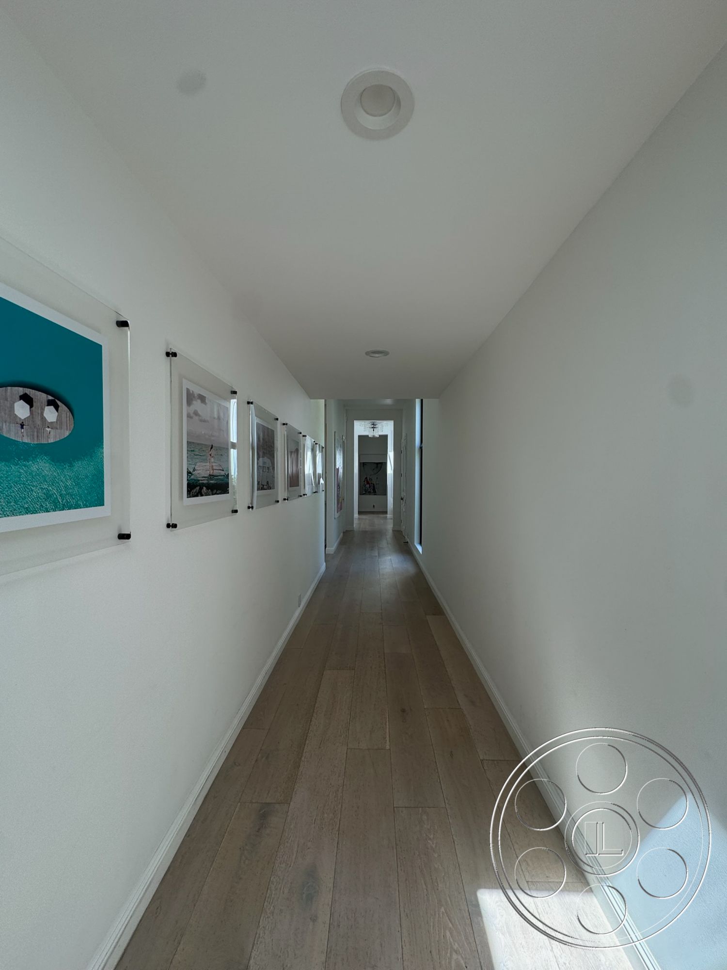 Modern 522 - light hardwood flooring, natural light from windows, recessed ceiling lights, interior hallway, white painted walls, framed artwork on walls, narrow hallway design