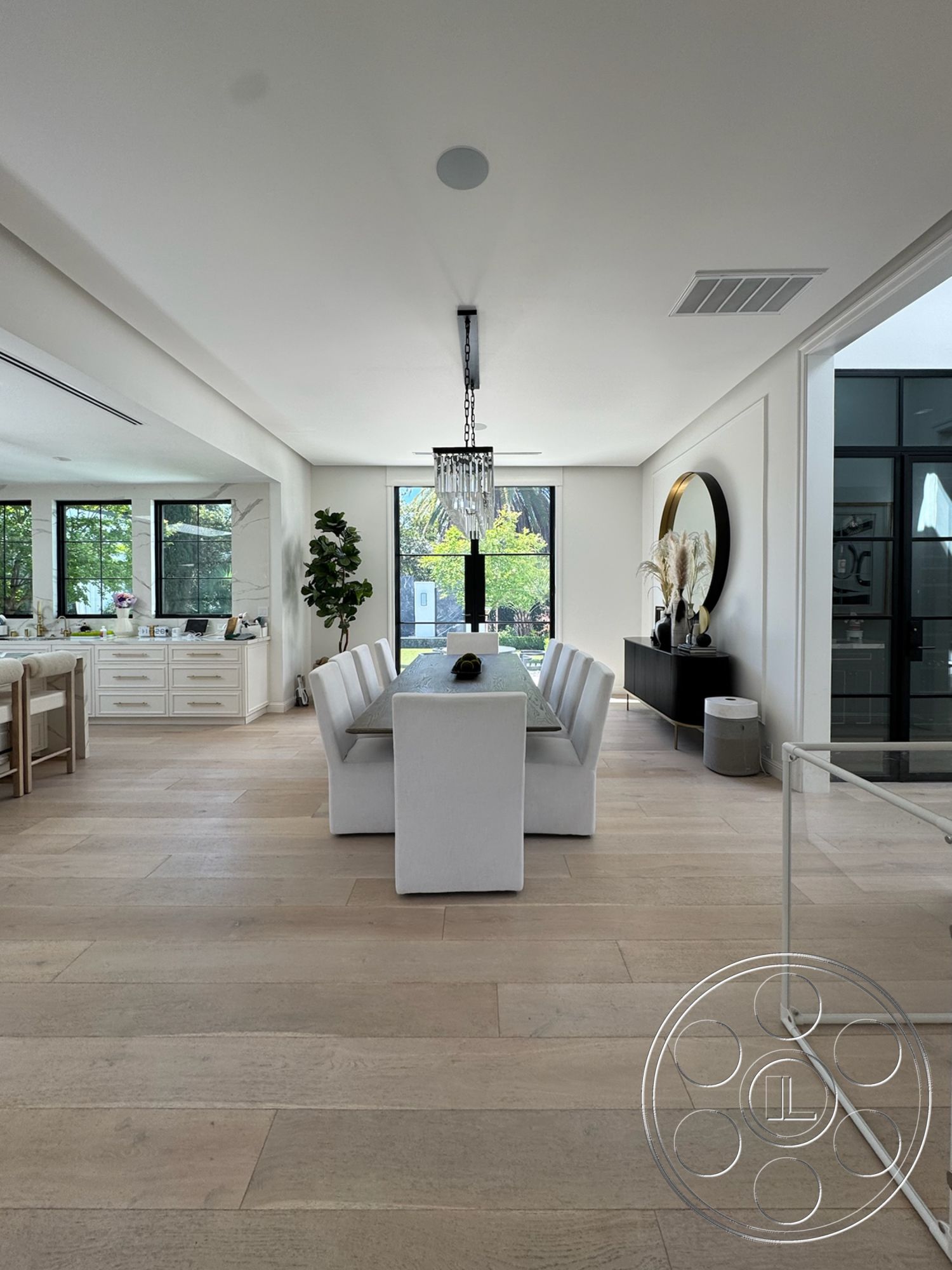 Modern 522 - high ceilings, minimalist decor, neutral wall colors, open floor plan, light wood flooring, chandelier lighting, textured ceiling, greenery visible through windows, elegant lighting fixtures, modern dining area, contemporary dining table, built-in white cabinets, round decorative mirror, white upholstered dining chairs, glass windows with black frames