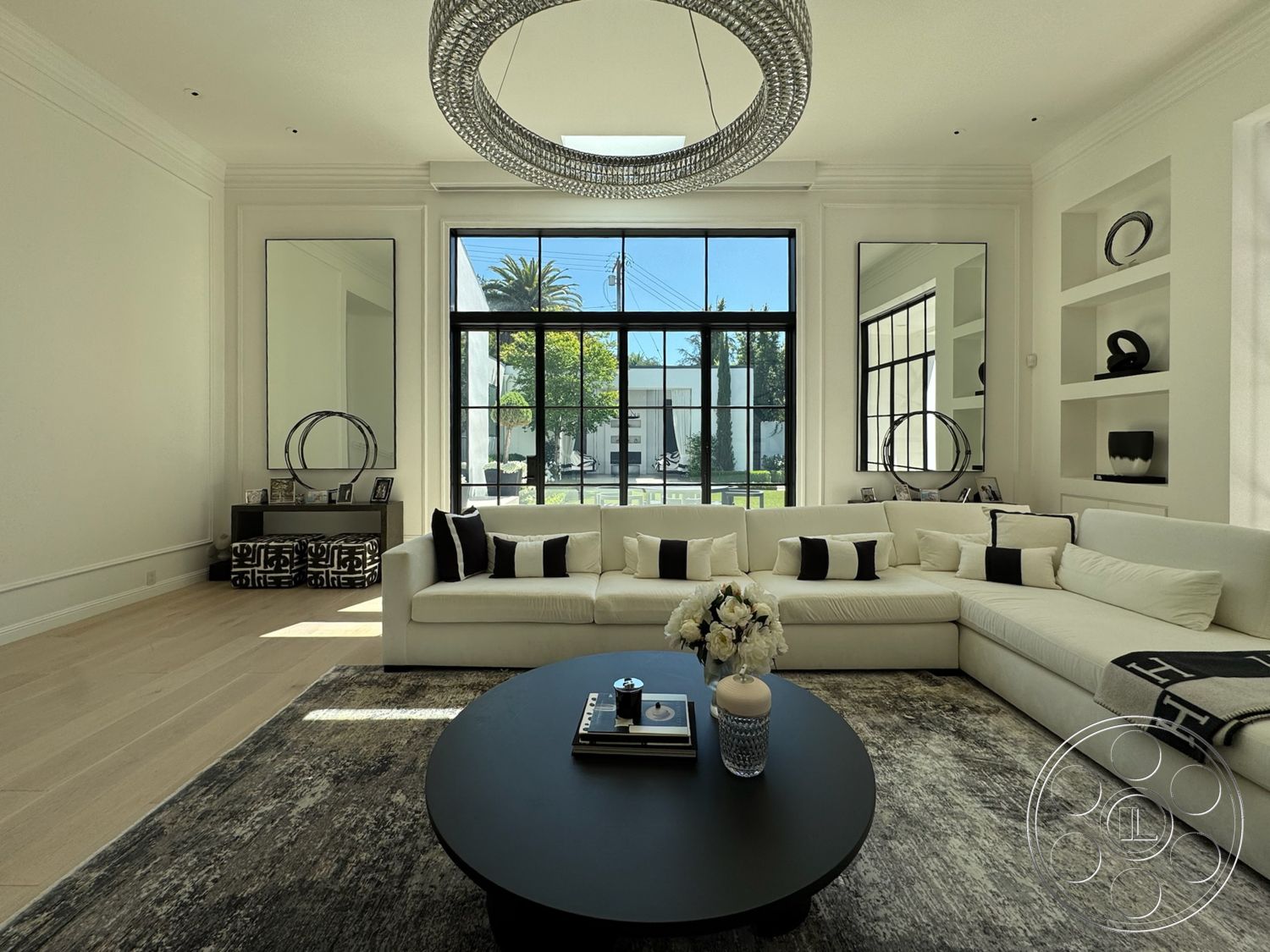 Modern 522 - modern chandelier, black circular coffee table, large floor-to-ceiling windows, hardwood living room floors, white painted walls, geometric patterned area rug, sectional sofa with white upholstery, black and white decorative accents, built-in shelves with minimalistic decor