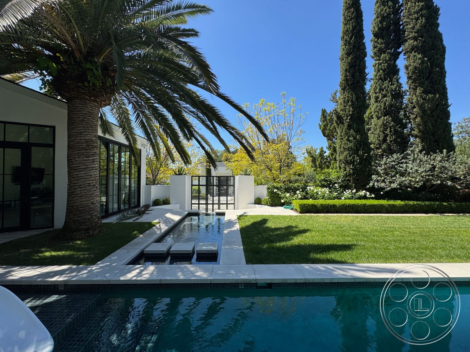 Modern 522 - exterior, landscaped garden, white stucco walls, modern architecture, glass doors, rectangular swimming pool, concrete pathway, outdoor living space, lush green grass, tall cypress trees, tropical palm trees, concrete pool deck, stone pool coping, sliding glass panels