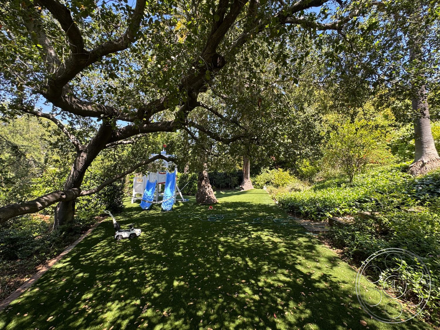 Modern 522 - exterior, lush greenery, flowering shrubs, large shade trees, natural landscape setting, artificial grass lawn, playground structure with slides, colorful play equipment, permeable garden edging