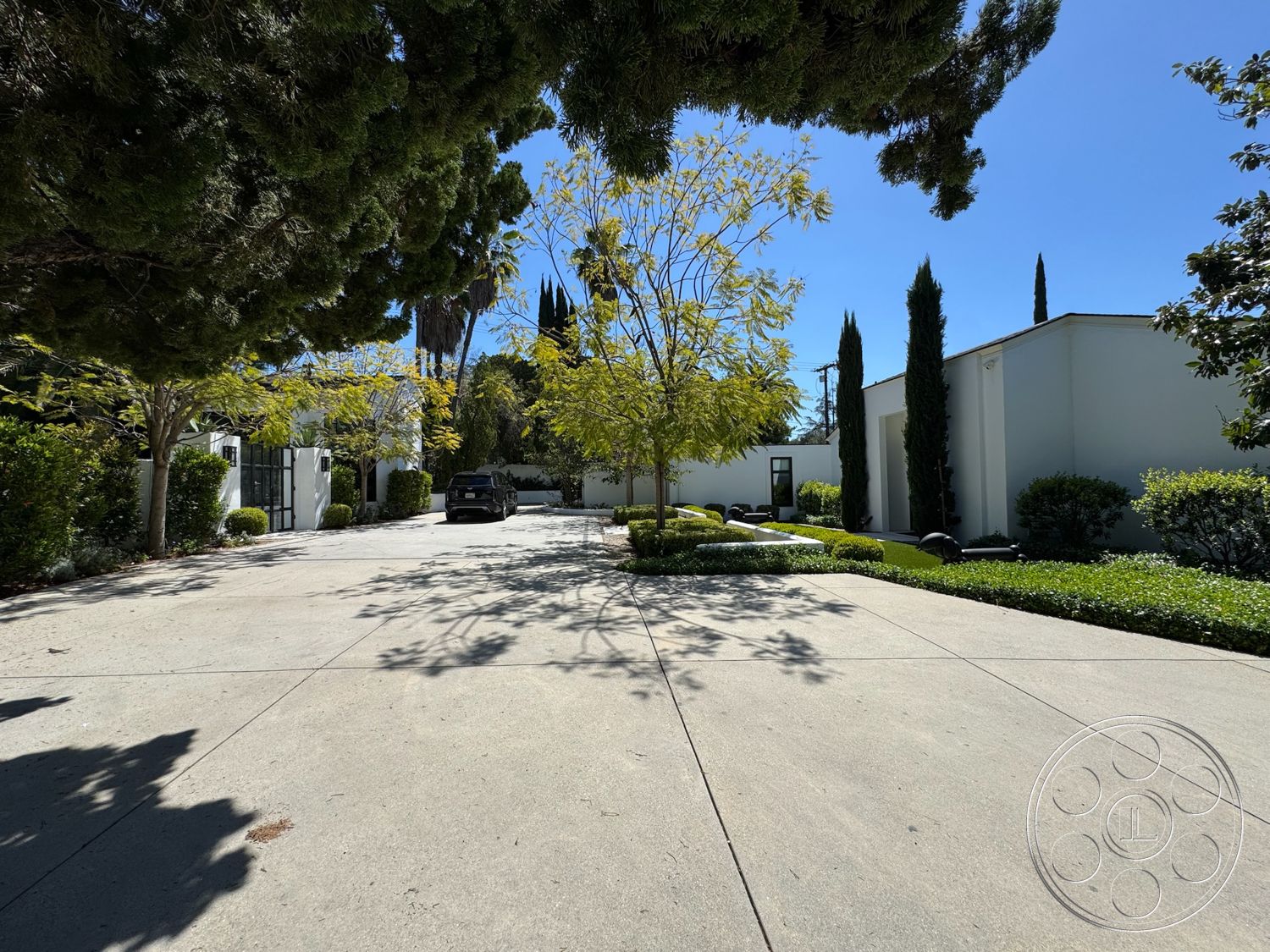 Modern 522 - white stucco walls, landscaped front yard, modern architectural style, concrete driveway, ornamental stones, planted flower beds, flat roof design, low-maintenance shrubbery, interior parking area, tall narrow cypress trees, exterior garden lighting