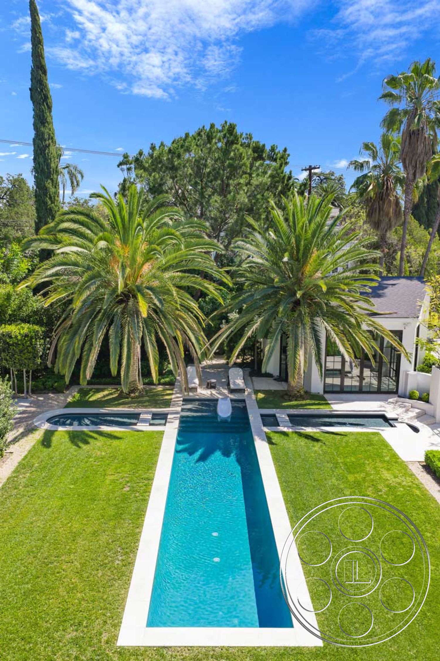 Modern 522 - exterior, lush green lawn, clear blue sky, landscape greenery, rectangular pool, concrete pool border, palm tree landscaping, symmetrical garden layout, modern house facade, slate patio area