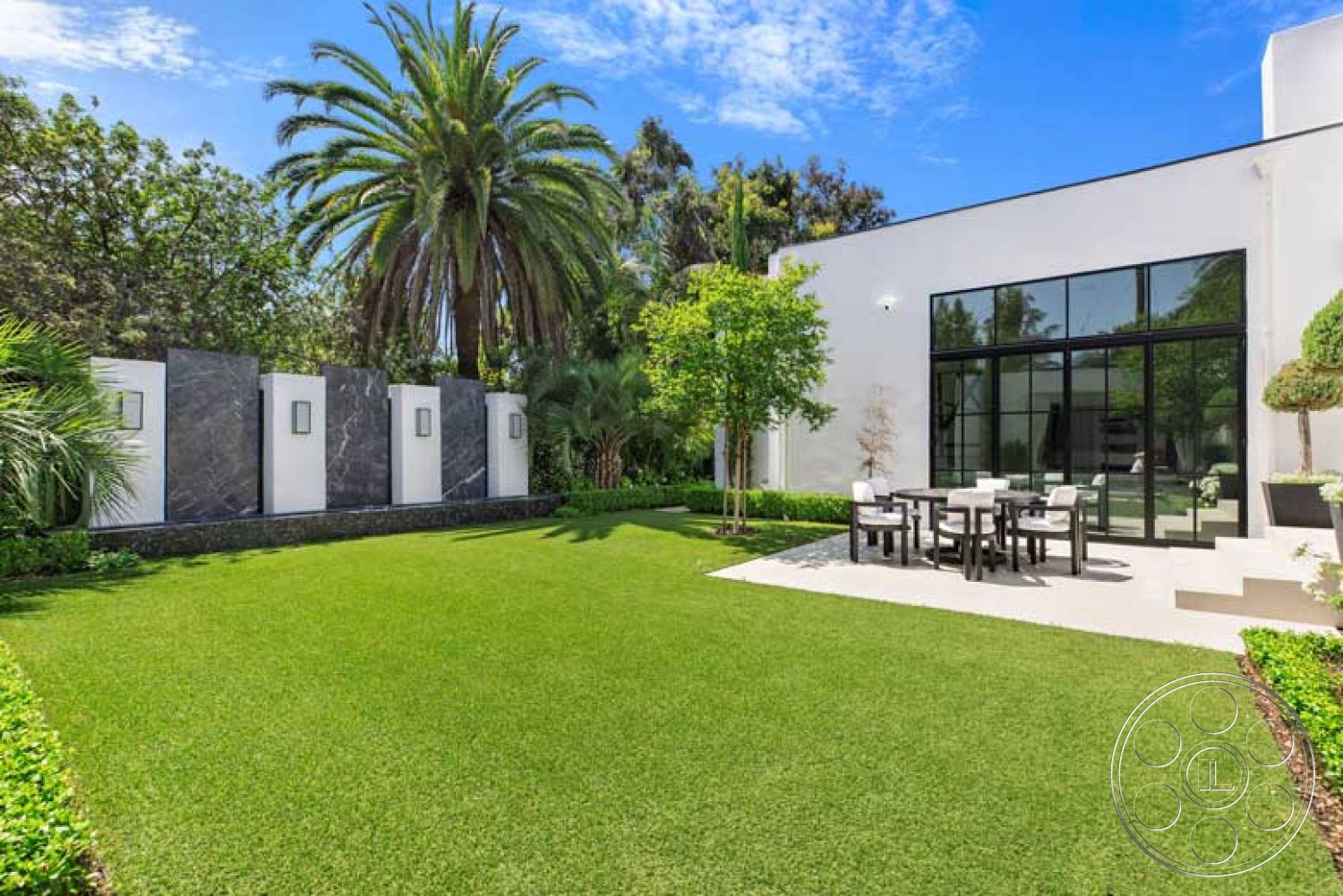 Modern 522 - exterior, landscaped garden, green grass lawn, flat roof design, concrete patio floor, modern glass sliding doors, palm tree accents, stone privacy wall, modern outdoor dining table, rectangular lawn area