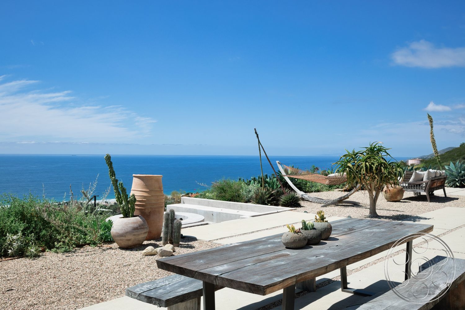 Modern 523 - exterior, wooden dining table, outdoor seating area, gravel landscaping, mountain backdrop, coastal setting, natural stone planters, hammock, concrete patio flooring, oceanfront view, modern architectural design, landscaped garden with succulents, ceramic garden pots