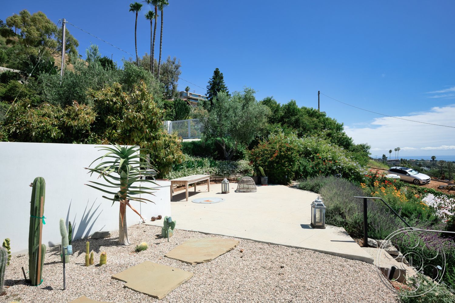 Modern 523 - exterior, wooden bench seating, gravel landscaping, mountain view, clear blue sky, desert plants, greenery backdrop, hillside location, cactus garden, stepping stone pathway, concrete patio floor, colorful flowering shrubs