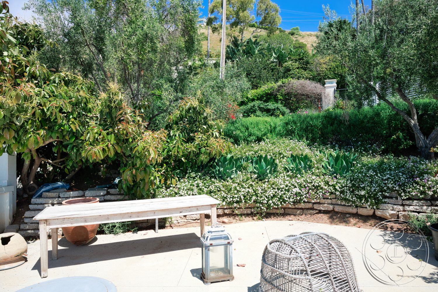 Modern 523 - exterior, lush greenery, wooden bench, terracotta planter, circular garden layout, concrete patio flooring, woven outdoor chair, stone landscape border, flower bed with mixed plants, stone wall terrace