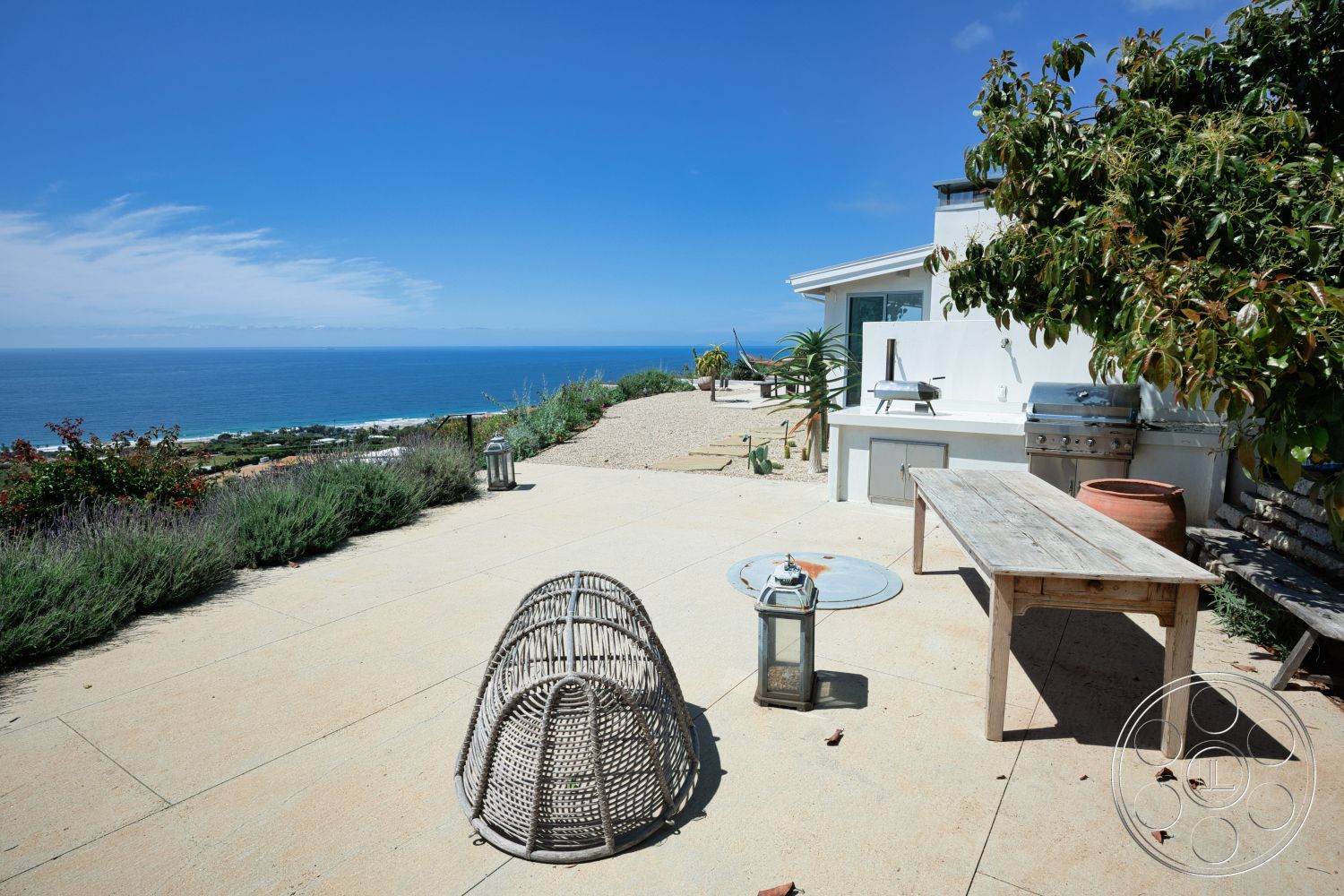 Modern 523 - natural light, exterior, blue sky, sea view, woven rattan chair, concrete patio flooring, wooden outdoor dining table, minimalist outdoor setting, stone barbecue grill area, landscaped garden with lavender